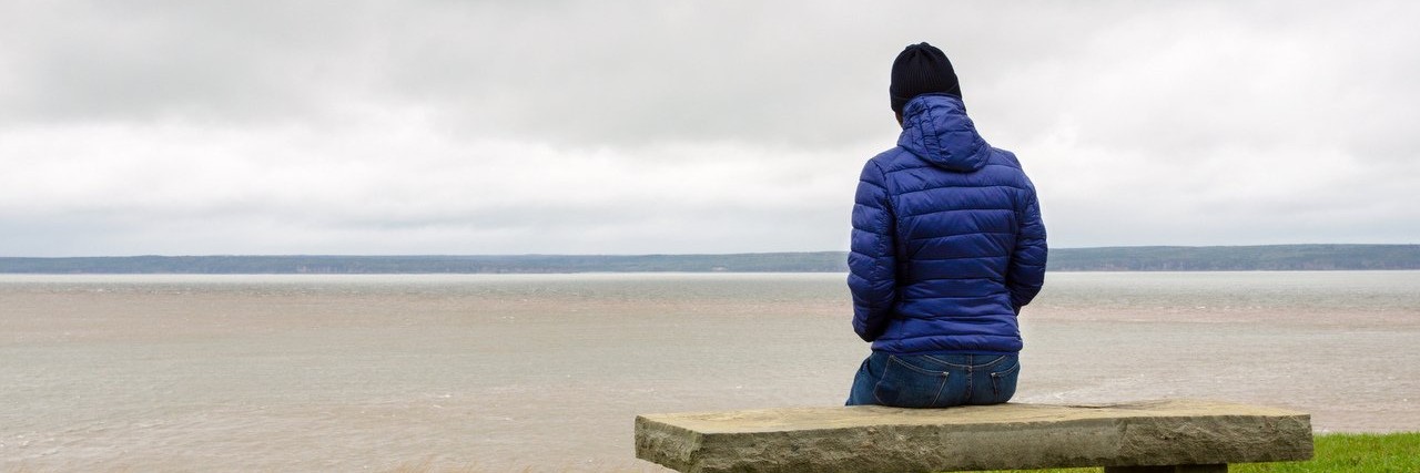 Woman Wants People to Understand Her Complex Regional Pain Syndrome woman sitting on a bench in front of the sea