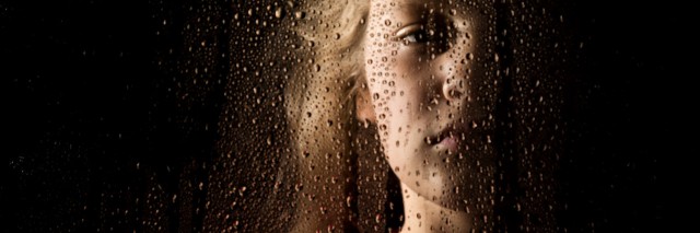 solemn young woman behind the window with drops.
