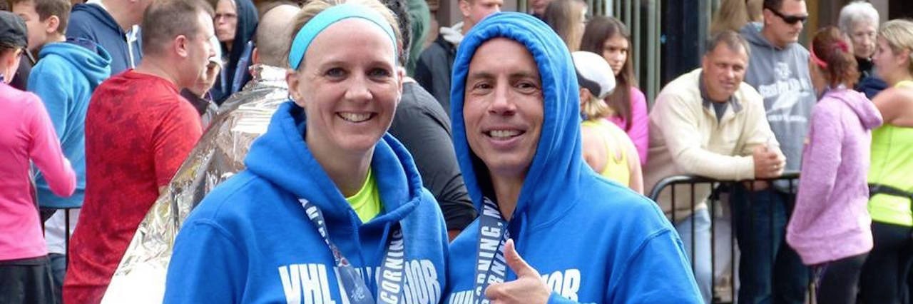 Running as a Von Hippel-Lindau Syndrome (VHL) Warrior husband and wife wearing blue hoodies and medals after running a race
