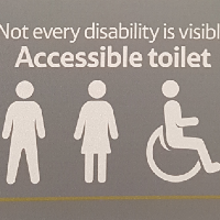 Image of a Tesco bathroom sign which says "not every disability is visible. Accessible toilet." and then shows the symbols for a man, woman and wheelchair sign.