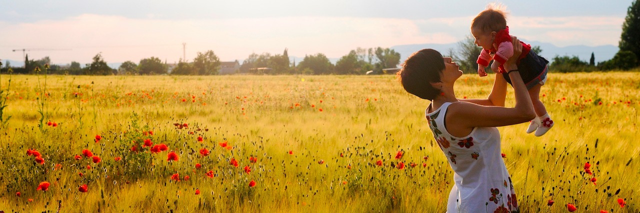 How I Found Positivity and Acceptance After Postpartum Depression A woman holding up her child in a field of flowers