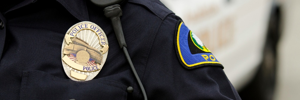 a close up of an officers uniform and badge with a patrol car in the background