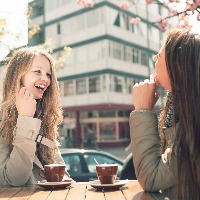 Two women laughing together while drinking coffee at a cafe