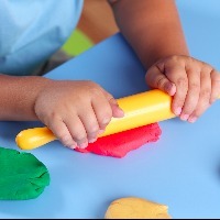 Child with rolling pin playing with play dough on a table