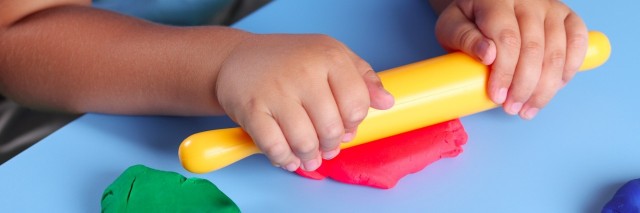 Child with rolling pin playing with play dough on a table