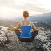 woman sitting on a rock in a meditation pose looking out at mountains and valley