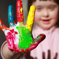 Girl with Down syndrome. Her hand is covered in rainbow paint.