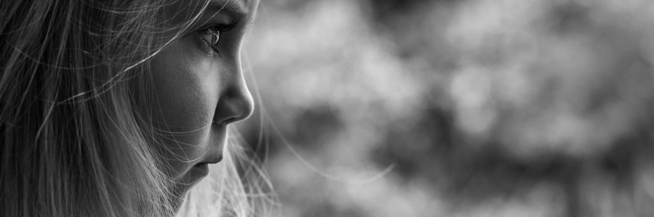 What It's Like Growing Up With Fibromyalgia Black and white gritty image of preschooler girl looking forward with a frustrated expression