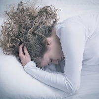 woman lying in bed holding head