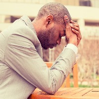 side profile young businessman sitting outside corporate office holding head with hands looking down