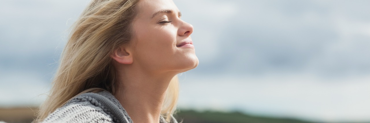 Slowing Down and Living in the Moment With Illness young woman with blonde hair closing her eyes, smiling and enjoying the sunshine