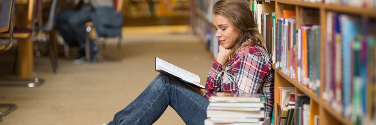 Student reading book on library floor.