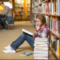 Student reading book on library floor.