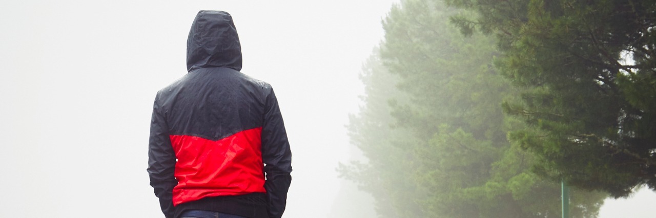 Man walking next to trees, wearing a jacket on a foggy day