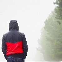 Man walking next to trees, wearing a jacket on a foggy day