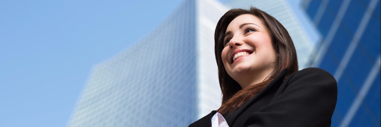 businesswoman smiling and standing in front of a skyscraper