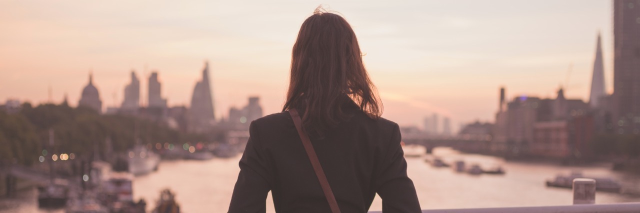 woman standing on a bridge at sunrise looking at a river and a city