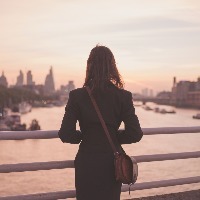 woman standing on a bridge at sunrise looking at a river and a city