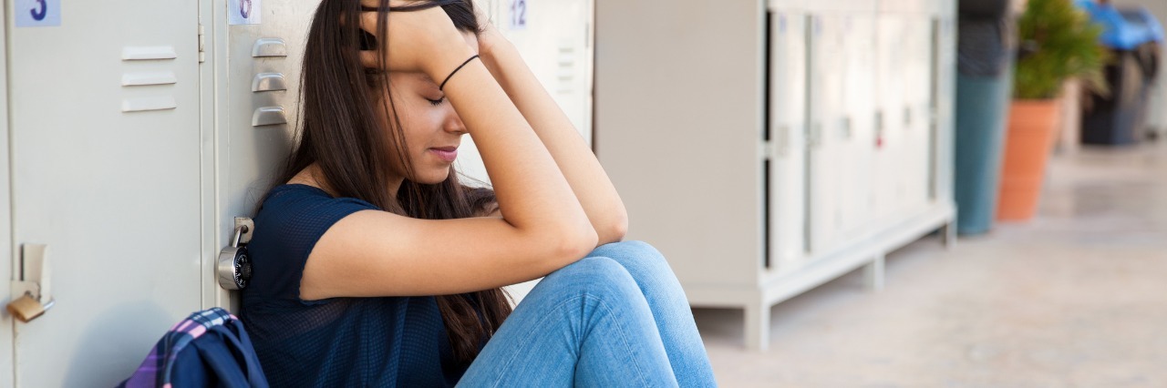 Being a Teenager With Fibromyalgia teenage girl sitting by the lockers next to her backpack with her head in her hands