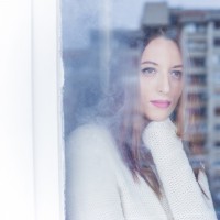 Beautiful young woman looking through the window on a winter day.