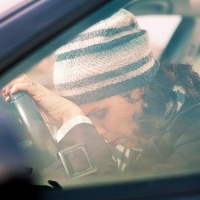 sad and tired woman leaning her head on the steering wheel while sitting in the car