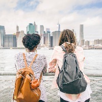women wearing backpacks standing on bridge looking at skyline