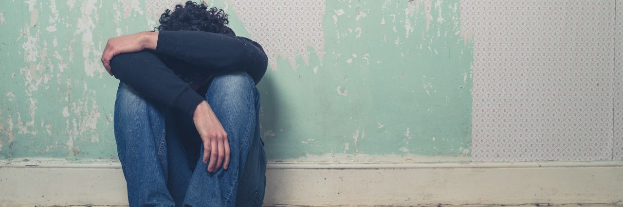 Low Cortisol and Feeling Emotions With Chronic Fatigue Syndrome A sad and depressed young man is sitting on the floor in an empty room