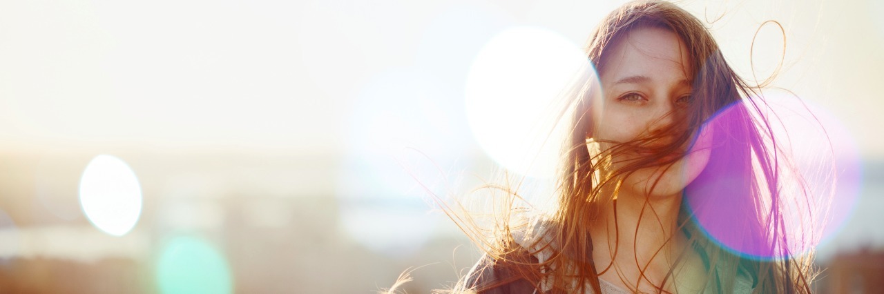 Young Woman Standing in Sunset Light, Looking at Camera. Hair Fluttering in the Wind. Selective Focus,