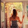 A young woman is standing in the doorway of her kitchen and is looking at the garden at sunrise