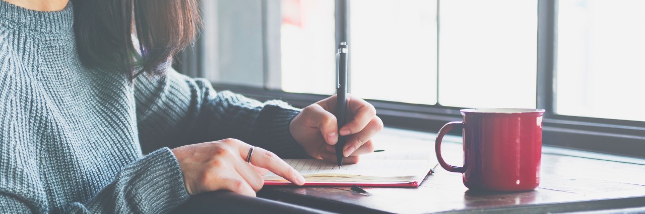 Why I Write About My Borderline Personality Disorder woman writing in notebook with cup of coffee on table