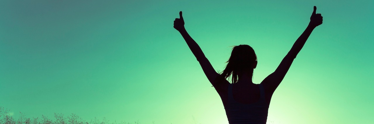How I Managed My Anxiety at Work A woman sitting in a field of grass with her hands in the air