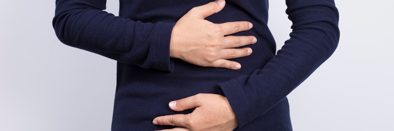 What I Have Learned About Ulcerative Colitis woman in dark blue shirt holding her stomach