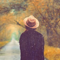 Woman wearing hat walking down tree-lined path