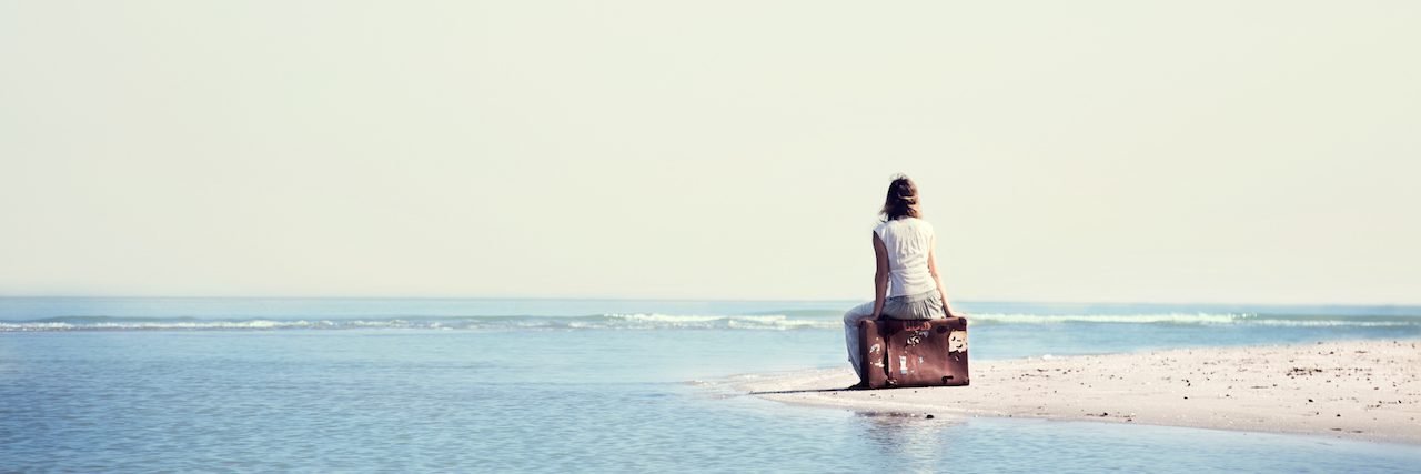 A woman sitting on a bag, looking at the ocean