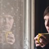 Lonesome woman drinking cup of coffee by the window of her living room