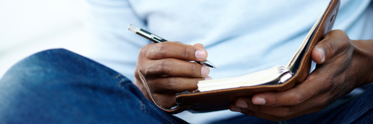 Hands of young man writing something in notepad
