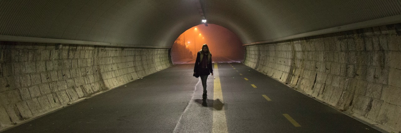 young lady walks alone trough a tunnel in the night