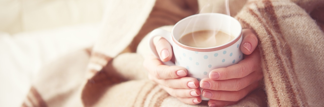 woman's hands holding warm mug of coffee. she is wrapped in a warm heavy blanket