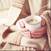 woman's hands holding warm mug of coffee. she is wrapped in a warm heavy blanket