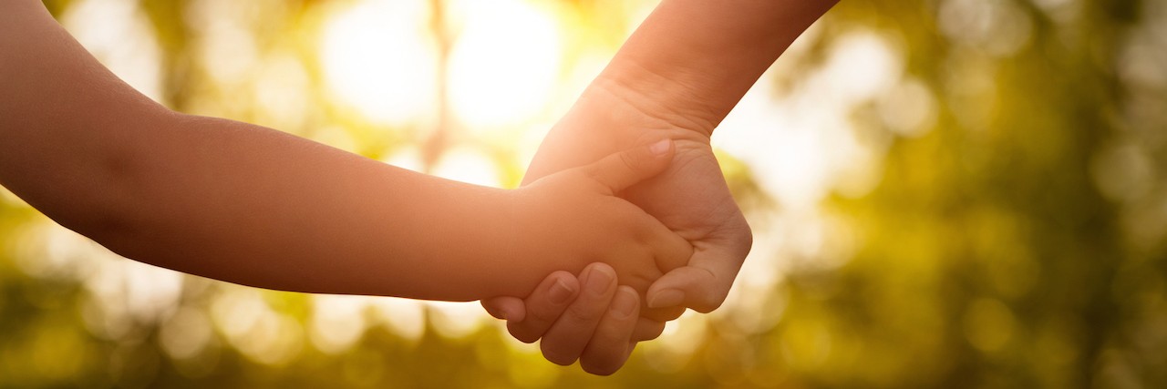 Close up of mother or older sister and a child hands at the sunset