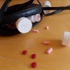 Three pill bottles, one of which is open, and red and pink pills spill out from a black handbag with a twisted strap.