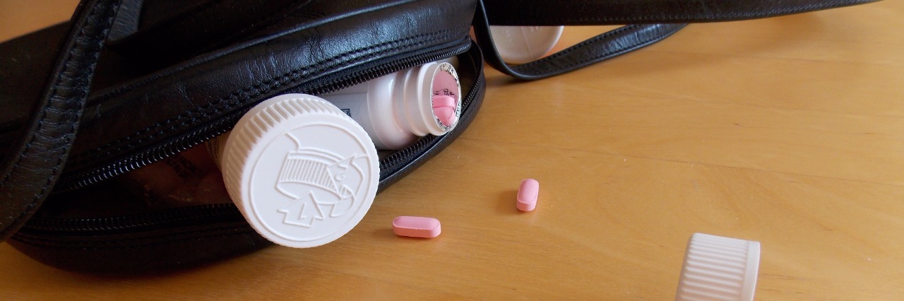 To the Man at the Party Who Saw My Pain Medications Three pill bottles, one of which is open, and red and pink pills spill out from a black handbag with a twisted strap.