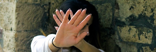 woman holding her hands up in front of her face and looking away in front of stone wall