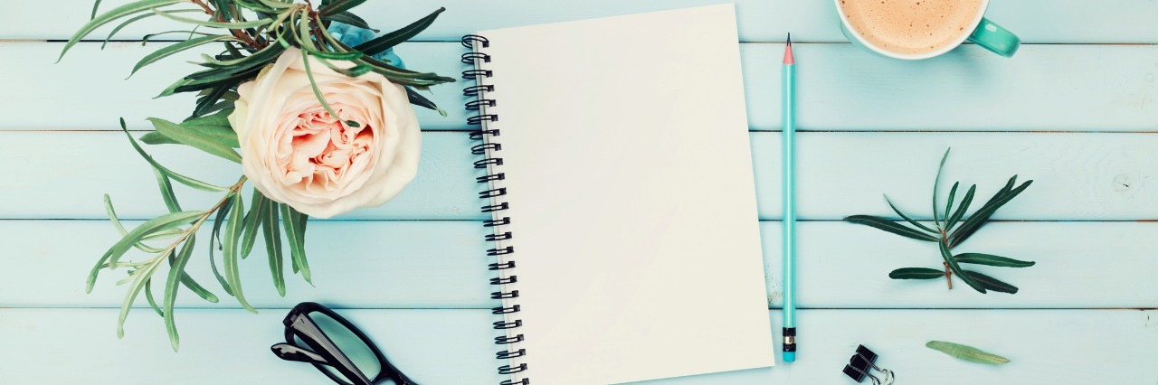 Morning coffee cup, clean notebook, pencil, eyeglasses and vintage rose flower in vase on