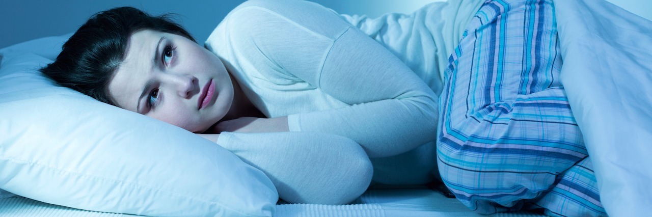 PTSD: The Monsters Under Your Bed in Adulthood a woman lying down, looking scared in bed