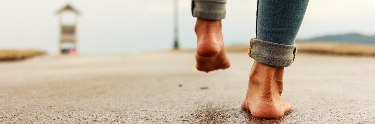 How I'm Getting My Legs Back After a Rare Dystonia Diagnosis Woman walking barefoot down a path.