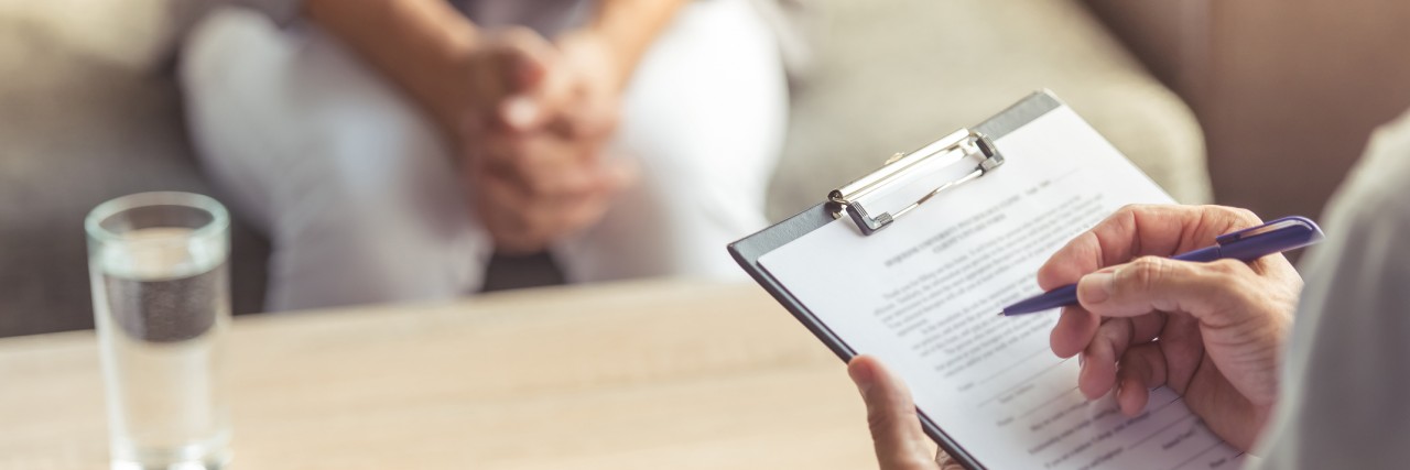 Cropped image of depressed man at the psychotherapist. Doctor is making notes while listening to his patient