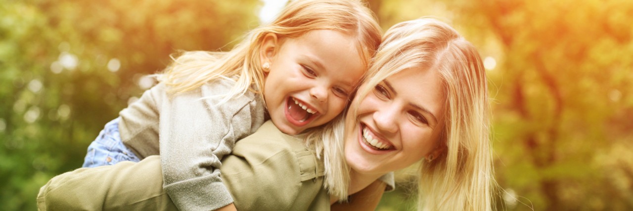 Multiple Sclerosis: Teaching Children Body Positivity as a Mother mom gives a piggy back ride to her young daughter outside