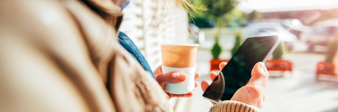 Woman using smart phone and holding coffee outdoor