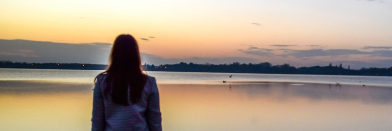 Woman standing in front of lake at sunset